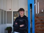 Man in zwarte trui leunt tegen blauwe paal