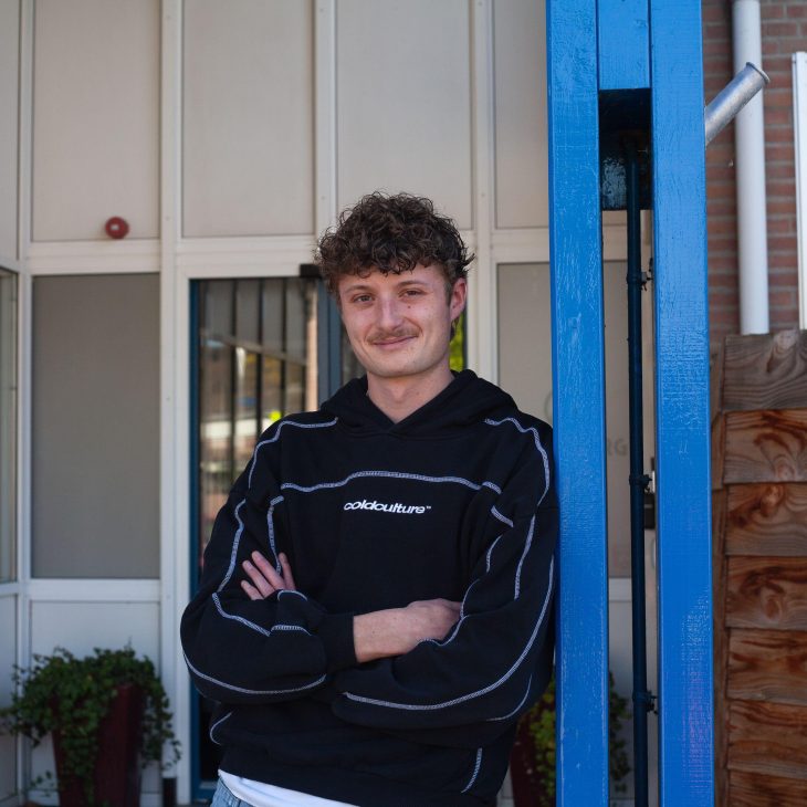 Man in zwarte trui leunt tegen blauwe paal