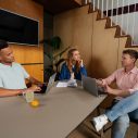 Drie zorgprofessionals die samen aan een tafel zitten te werken aan een project.