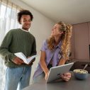 Man met boek in hand kijkt naar vrouw met tablet