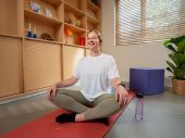Vrouw in wit tshirt zit op oranje yoga mat in kleermakerszit