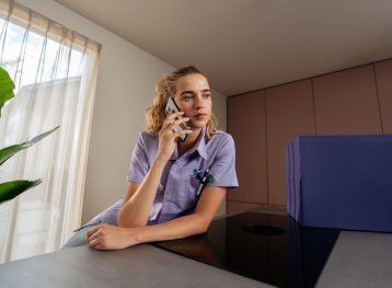 Een vrouwelijke zorgprofessional. Ze is aan het bellen en heeft een neutrale blik.