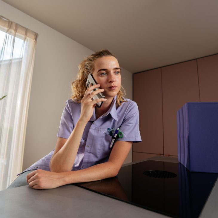Een vrouwelijke zorgprofessional. Ze is aan het bellen en heeft een neutrale blik.