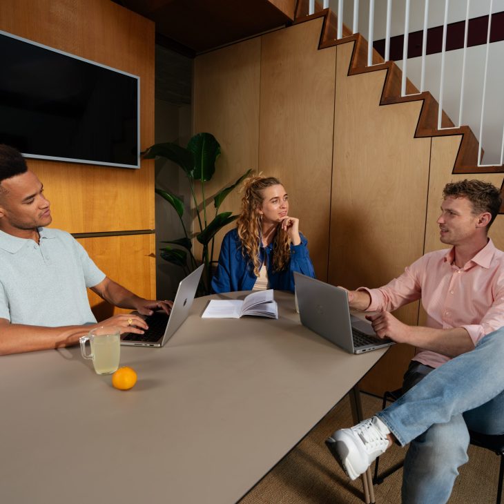 Drie zorgprofessionals die samen aan een tafel zitten te werken aan een project.