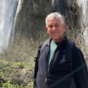 Man met grijs haar en zwarte jas, portret in natuurlijke omgeving