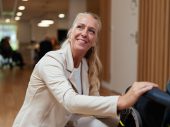 Een persoon in wit uniform biedt hulp aan iemand in een rolstoel in een moderne binnenruimte met houten vloer en sfeerverlichting