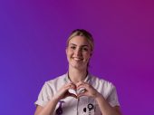 Een zorgprofessional in wit uniform maakt een hartvorm met de handen tegen een paarse en roze achtergrond