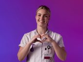 Een zorgprofessional in wit uniform maakt een hartvorm met de handen tegen een paarse en roze achtergrond