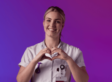 Een zorgprofessional in wit uniform maakt een hartvorm met de handen tegen een paarse en roze achtergrond.