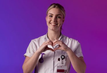 Een zorgprofessional in wit uniform maakt een hartvorm met de handen tegen een paarse en roze achtergrond