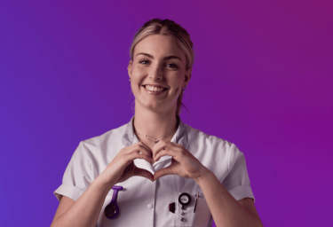 Een zorgprofessional in wit uniform maakt een hartvorm met de handen tegen een paarse en roze achtergrond.