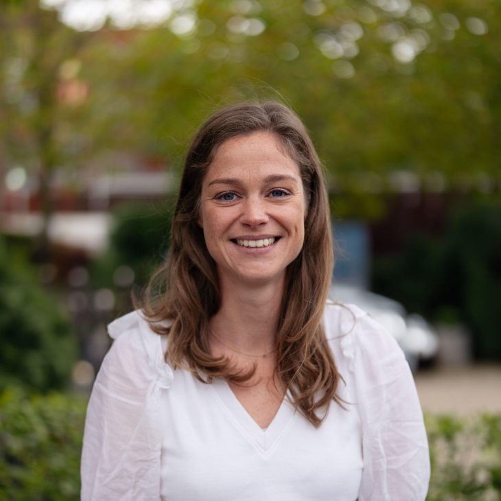 Foto van vrouw met lang bruin haar in witte blouse in natuurlijke omgeving