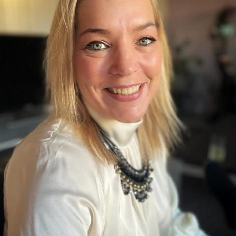 vrouw met halflang blond haar, witte blouse en halsketting