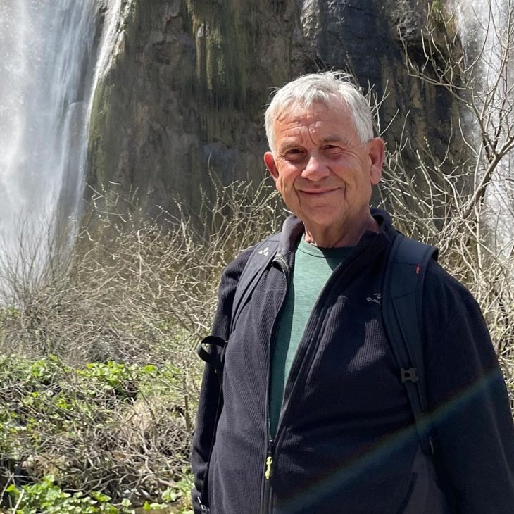 Man met grijs haar en zwarte jas, portret in natuurlijke omgeving