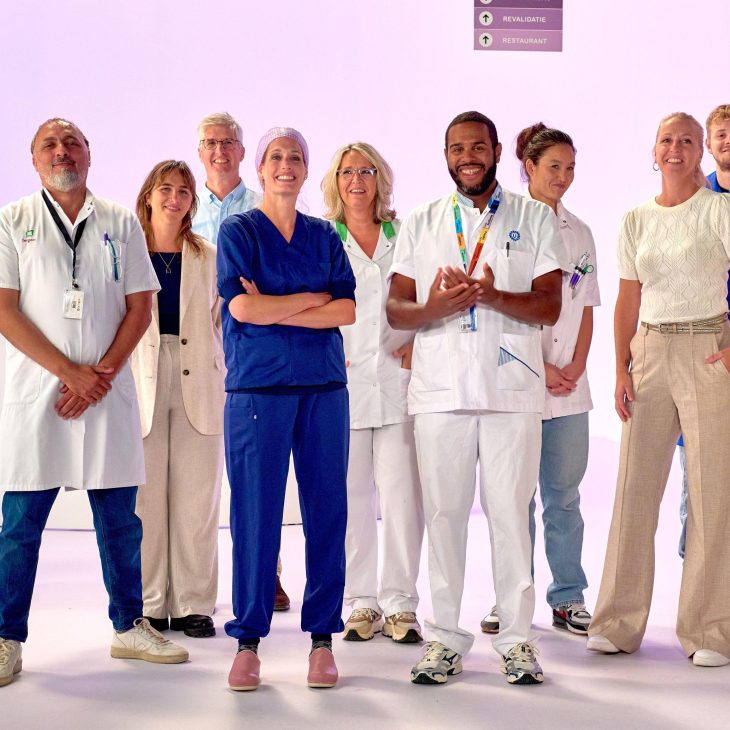 Een groep van negen zorgmedewerkers staan geposeerd voor een lichtpaarse achtergrond