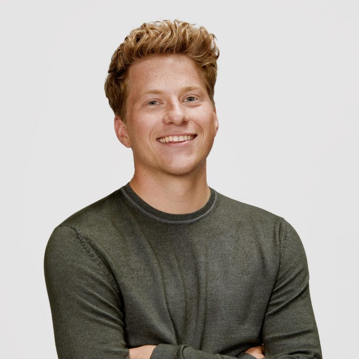 Portretfoto van een jonge man, kort haar en een donker shirt met lange mouwen voor een witte achtergrond