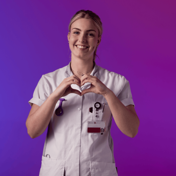 Een zorgprofessional in wit uniform maakt een hartvorm met de handen tegen een paarse en roze achtergrond.