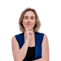 Een blonde vrouw die kracht uitstraalt houd haar hand voor haar gezicht alsof ze een idee heeft, draagt een donker blauw gilet.