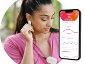 Een vrouw met een roze shirt aan heeft in aan haar kleding de HearthMath inner balance trainer hangen. Daarnaast staat een mockup van een telefoon waarop de app van Inner Balance Trainer open staat.