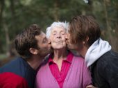 Een oudere vrouw die zoenen op haar wang krijgt van twee andere mensen