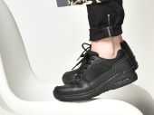 Een persoon staat op een stoel, alleen de schoenen zijn zichtbaar. Het zijn zwarte sneakers en deze persoon staat op zijn tenen.