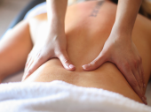 Een persoon ligt op z'n buik op een massagebed. De rug is ontbloot en er zijn twee handen die de rug masseren.