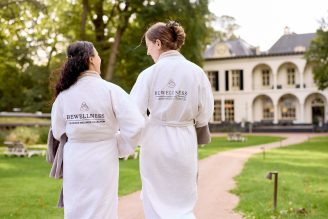 Twee vrouwen lopen in badjassen over een grind pas op een wellnessresort