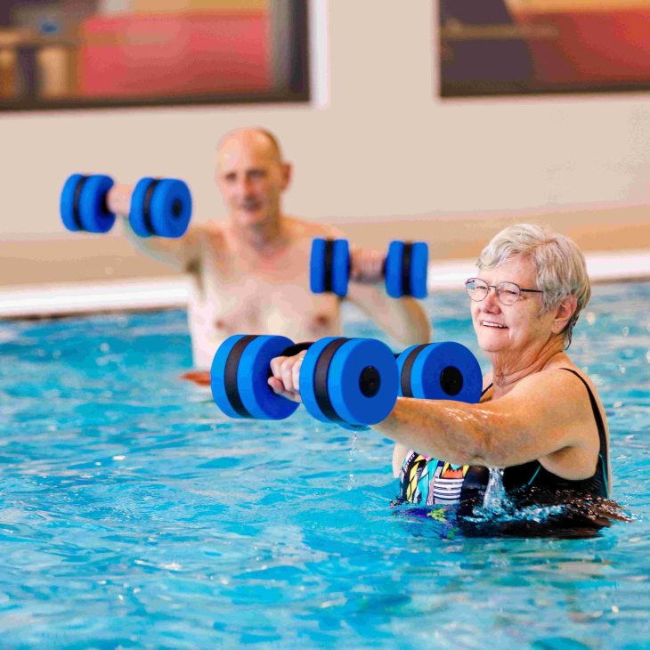 Twee personen staan in een zwembad en volgen een aquafit-les, ieder met gewichten in hun handen.