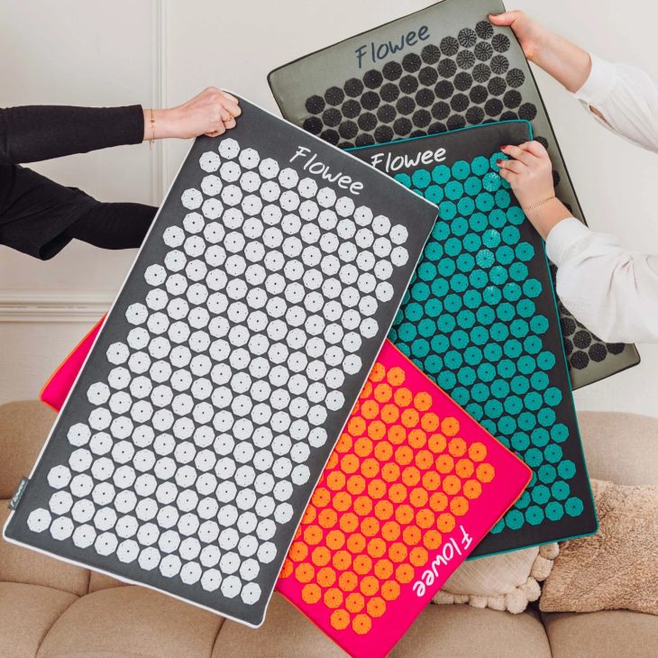 Vier verschillende grote en gekleurde spijkermatten die 3 paar armen vasthouden. Op de achtergrond zie je een beige bank met kussens.