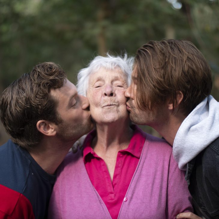 Een oudere vrouw die zoenen op haar wang krijgt van twee andere mensen