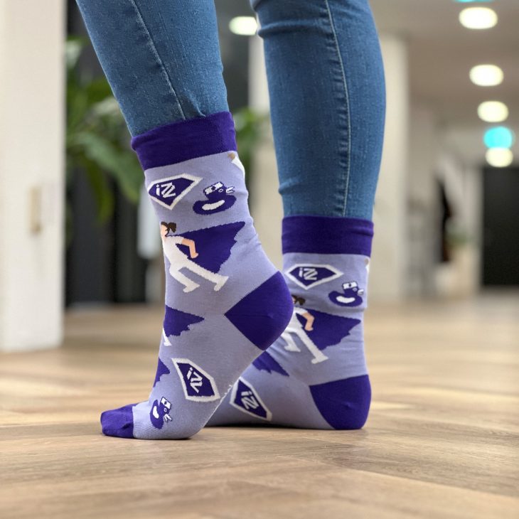Paarse IZZ zokken, aan 2 voeten. Model draagt de sokken over spijkerbroek