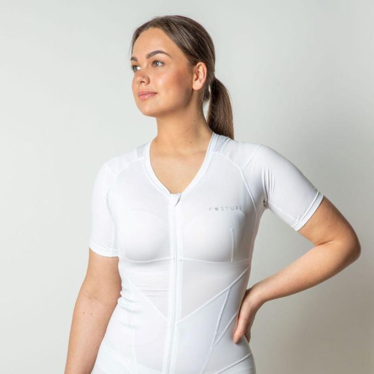 Vrouw kijkt naar links heeft een wit houdingshirt aan. En heeft haar linkerarm in haar zij.