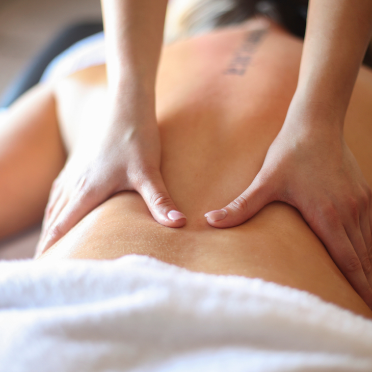 Een persoon ligt op z'n buik op een massagebed. De rug is ontbloot en er zijn twee handen die de rug masseren.