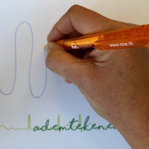 Hand met oranje pen tekent slingers. Eronder staat ademtekenen in het groen geschreven