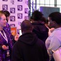 Meerdere mensen zijn met elkaar in gesprek bij een stand op een beursvloer van IZZ.