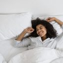 Lachende vrouw rekt zich uit in een wit bed
