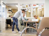 Man in spijkerbroek leunt op tafel, overleg met andere man in zorgsetting
