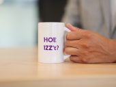 Hand houdt witte mok vast met paarse tekst: Hoe IZZ't?