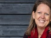 Portret van vrouw kijkend naar camera. Achtergrond grijze planken