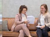 Twee vrouwen kijken naar papieren zittend op een bruine bank