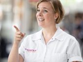Vrouw in zorgoutfit wijst met linkerwijsvinger