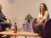 2 vrouwen zittend op paarse stoelen kijken naar de camera