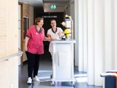 2 vrouwen lopen voor en naast kar in ziekenhuis