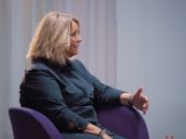 Vrouw in interview setting zit op paarse stoel
