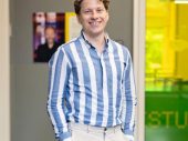 Man in blauw wit overhemd voor gele deur