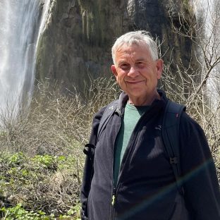 Man met grijs haar en zwart vest voor waterval