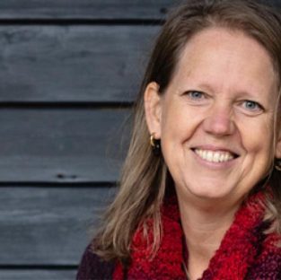 Portret van vrouw kijkend naar camera. Achtergrond grijze planken