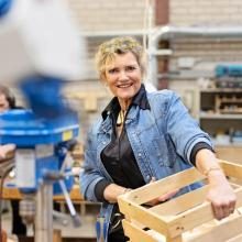 Vrouw met blond haar en spijkerjas die een licht houten krat vasthoudt