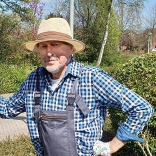 Man met hoed en ruitblouse rust op stok.