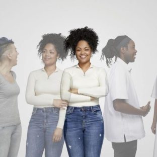 Groep mensen in zorg- en casual kleding kijkt naar elkaar, terwijl vrouw in het midden glimlachend recht vooruit kijkt.